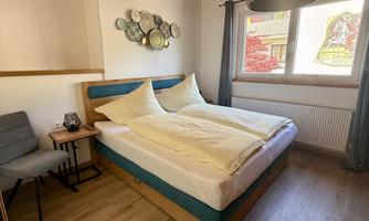 A cozy bedroom with a large bed and two pillows. The room has wooden ceilings and a simple desk chair.