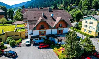 A cozy hotel in a green landscape, surrounded by mountains. Parking is available in front of the building.