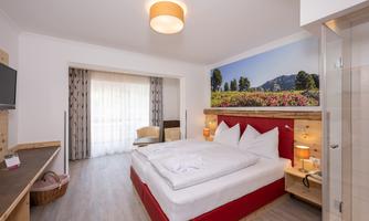 A modern bedroom with a large bed, wooden furniture, and a beautiful view of the landscape. The room is bright and inviting, with curtains and a flat-screen TV.