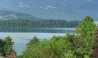 A beautiful landscape with a clear lake and surrounding mountains. Green trees frame the view.