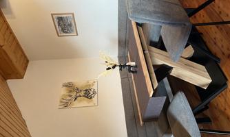 An inviting dining area with a wooden table and a gray upholstered corner sofa. Pictures hang on the wall and a flower stands as decoration on the table.