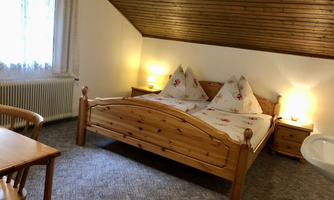 A cozy bedroom with a double bed and wooden decor. There is a table and chairs as well as warm light from the night lighting.