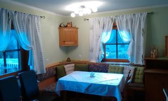 A cozy dining area with a table and a U-shaped bench. Bright curtains and windows create an inviting atmosphere.
