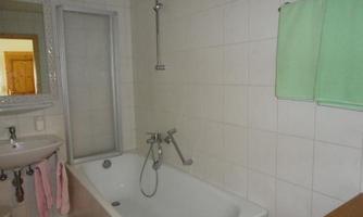 A simple bathroom with a bathtub and shower. A green towel and some bathroom accessories hang on the wall.