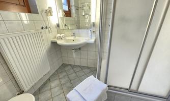 A modern bathroom with a sink, mirror, and shower. There are white tiles and a towel rack.