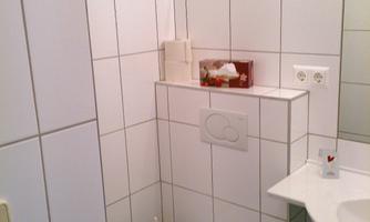 A small bathroom with white tiles and blue accents. It contains a toilet and a sink.