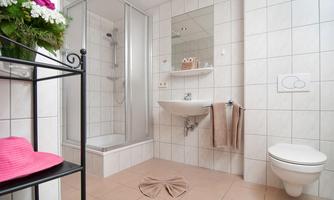 A modern bathroom with a shower cabin and bright tiles. Flowers are on a shelf and towels are neatly hung.