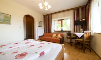 A cozy room with a large bed, a modern couch, and a table.  
Large windows provide plenty of daylight.
