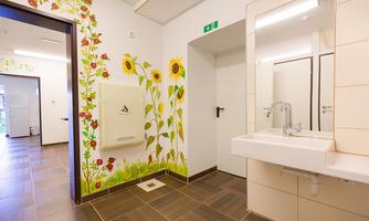 A bright bathroom with floral decoration on the walls. There is a sink and a towel dispenser.