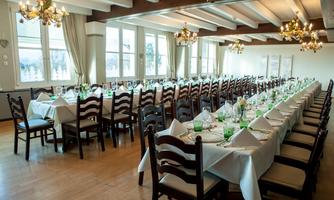 An elegant dining room with long tables and festive table decoration. Large windows provide plenty of daylight and a cozy atmosphere.