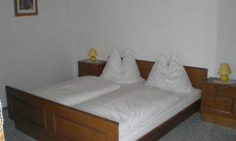 A simple bedroom with two single beds and familiar wooden furniture. There are two nightstands with yellow lamps and a picture on the wall.