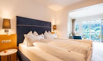 An elegant hotel room with two single beds and modern furnishings. The room features a balcony with a view of the greenery.