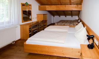 A cozy bedroom with wooden furniture and two beds. There is a table, chairs, and a mirror.