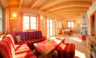 A cozy living space with a wooden ceiling and large windows. The decor consists of red sofas and a wooden table, perfect for social hours.