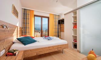A bright room with a comfortable bed and large windows that overlook a picturesque landscape. The decor is modern and inviting, with warm colors and wooden details.