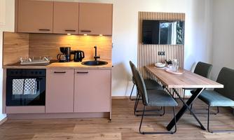 A modern kitchen with wooden cabinets and a dining table for six people. The decor is bright and friendly.