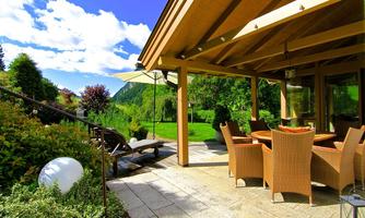 A beautiful terrace with a dining area and a spacious garden. The surroundings are green, and the clouds in the blue sky create a pleasant atmosphere.