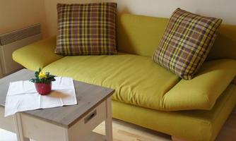 A cozy yellow sofa with checkered pillows stands next to a small table. The table has a blooming plant and a neatly folded white napkin on it.