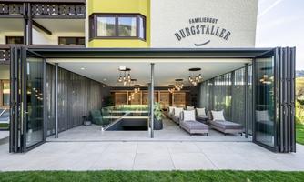 A modern, open living space with large glass windows. The room is elegantly furnished and offers a view of the green garden.