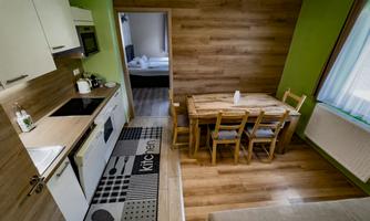 A modern kitchen with a wooden dining table and chairs. The walls are painted green, and there is plenty of natural light.