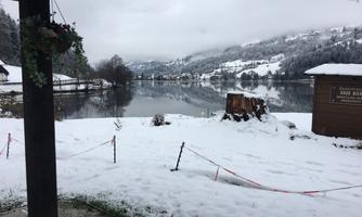 A snowy landscape with a tranquil lake in the background. The surrounding hills are covered in snow.