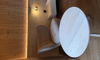A cozy armchair is positioned in a modern room with wooden paneling. The round table and gentle lighting create an inviting atmosphere.