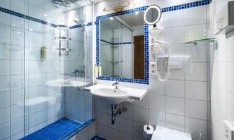 A modern bathroom with a shower and a sink. The walls are tiled in white and there is a large mirror.