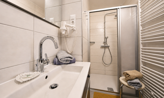 A modern bathroom with a large shower and a sink. Towels are placed on a chair and on the sink.