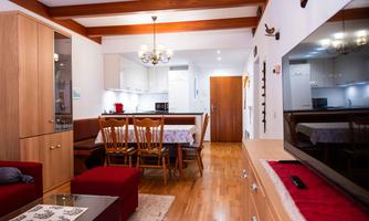 A cozy living room with a dining area and a modern kitchen. The decor is bright and inviting, with wooden furniture and a large television.