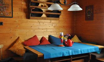 A cozy room with wooden paneling and a table in the center. The table is covered with a blue tablecloth and decorated with a teapot and colorful utensils.