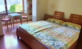 A cozy bedroom with a double bed and a small dining table. Light streams into the room through the window, and there is a beautiful view outside.