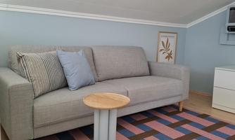 A modern living room with a grey sofa and a small side table. The floor is covered with a colorful rug in a geometric pattern.
