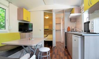 A modern mobile home with an open kitchen and living area. The space features bright colors, windows for plenty of light, and a cozy seating area.