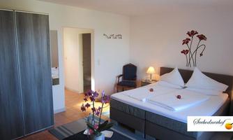 A cozy bedroom with a large bed and elegant white bedspreads. The room is modernly furnished and has a pleasant atmosphere with plant accents.
