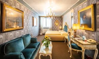 An elegant room with bright walls and a cozy seating area. The room is furnished with a double bed and decorative paintings.