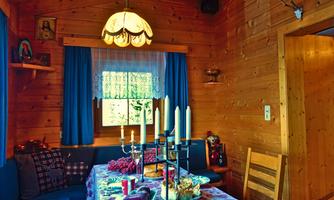 A cozy wooden room with a dining group and a table set with food. Bright curtains and a decorative lamp create an inviting atmosphere.