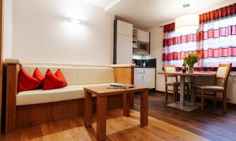 A cozy living area with a bright couch and red cushions. The table and chairs are near the kitchen, which is equipped with modern appliances.