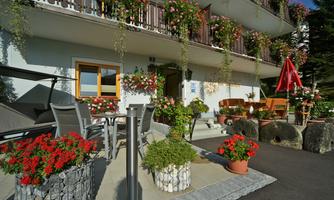An inviting building with balconies adorned with colorful flowers. Decorative plants and seating are located in front of the entrance.