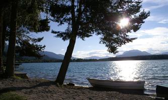 A calm lake with a boat on the shore. In the background, mountains and a clear sky can be seen.