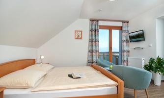 A cozy bedroom with a wooden bed and soft colors. The room features a window with a view outside and a comfortably furnished armchair.