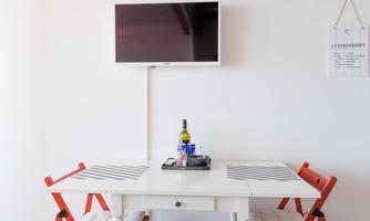 A cozy dining table with red chairs and a bottle of wine on it. A TV and a small chalkboard are hanging on the wall.