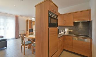 A modern kitchen with wooden cabinets and high-quality appliances. The space is bright and inviting, with a dining area and a couch in the background.