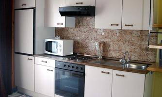 A practical kitchen with white cabinets and modern appliances. The space is bright and tidy, with a carpet on the floor.
