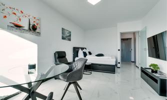 A modern room with a bed, a table, and chairs. The walls are light, and there are decorative pictures.