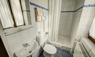 A small bathroom with a shower, a sink, and a toilet. Bright tiles and windows create a friendly atmosphere.