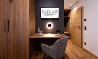 A modern room with a wooden desk, an elegant chair, and a television mounted on the wall. The warm wooden tones create a cozy atmosphere.