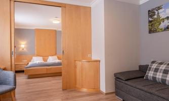 A cozy room with a sleeping area and a living room. The walls are light and the furniture is made of wood.