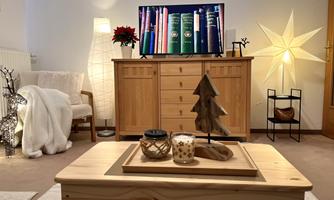 A cozy living room with a wooden cabinet and a television. On the table, there are candles and a little Christmas tree decoration.