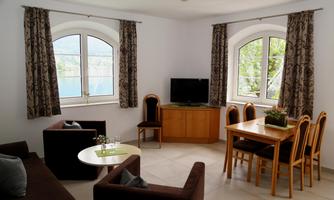 A bright living room with large windows and a beautiful view. The furnishings include a sofa, a dining table, and a television.