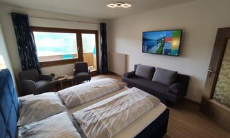 A cozy hotel room with two single beds and a wall-mounted TV. Through the window, there is a view of nature.